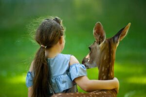 girl wearing blue top with her hand around a deer