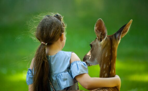 girl wearing blue top with her hand around a deer