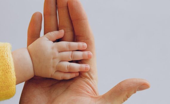 crop person touch palms with newborn baby on gray backdrop
