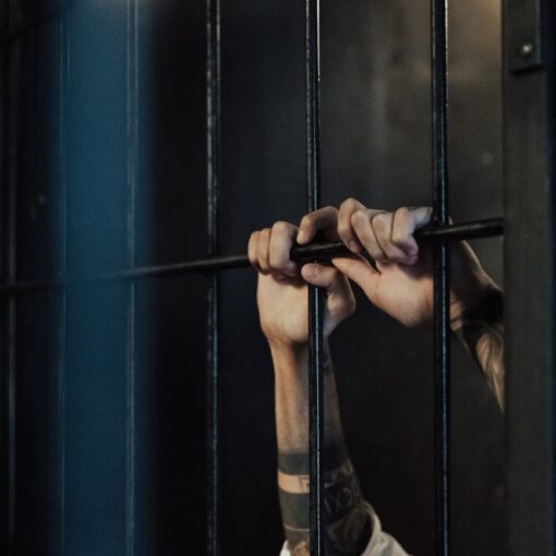 hands of a person holding on metal railings in a jail