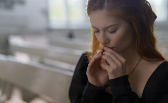 a woman in black long sleeves praying with her eyes closed
