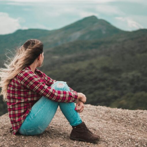 side view photo of woman sitting on ground overlooking a hill