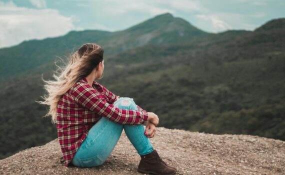 side view photo of woman sitting on ground overlooking a hill