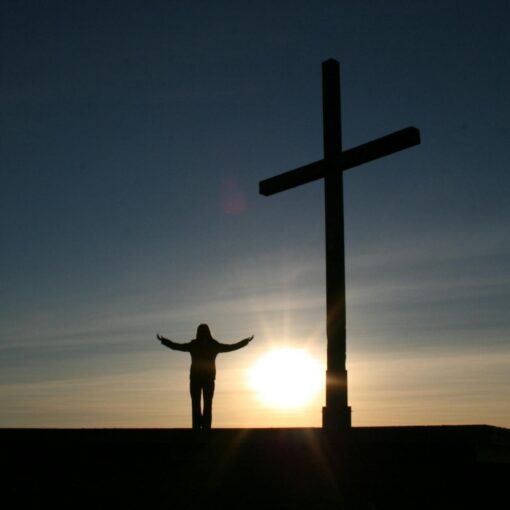silhouette of person standing beside cross during sunset