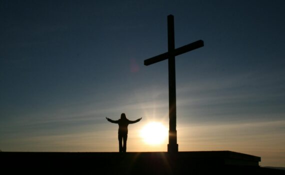 silhouette of person standing beside cross during sunset